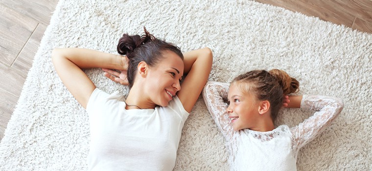 Mother and daughter wearing white tops whilst laying on a carpeted floor.