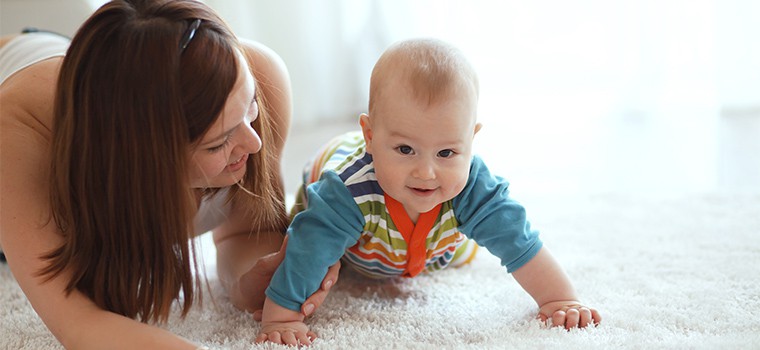 Mother holding her baby on the floor looking at the camera.