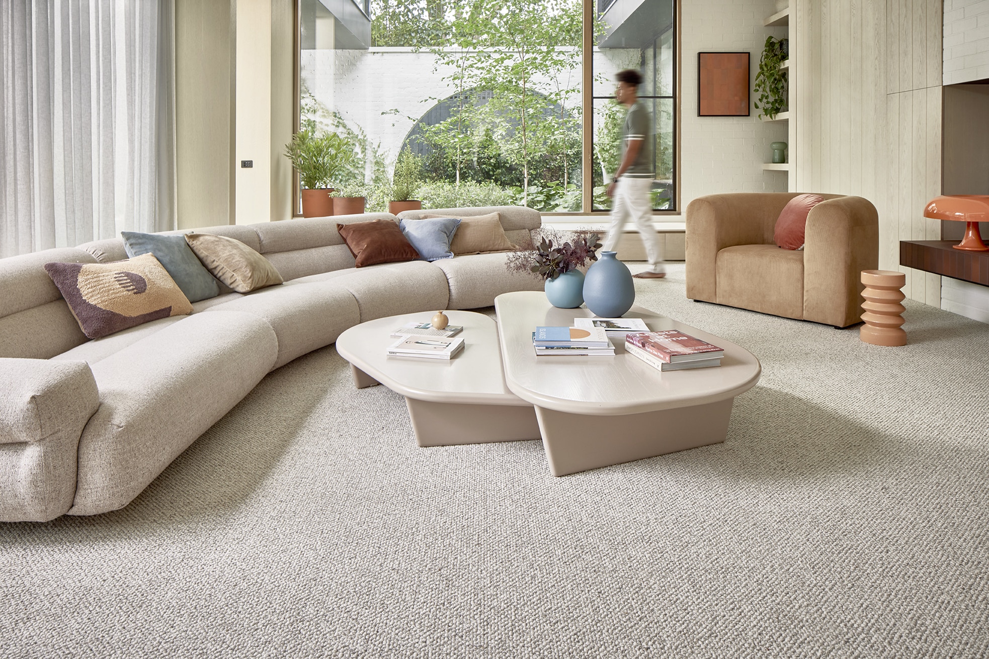 a living room with a large round couch and a man walking on carpet